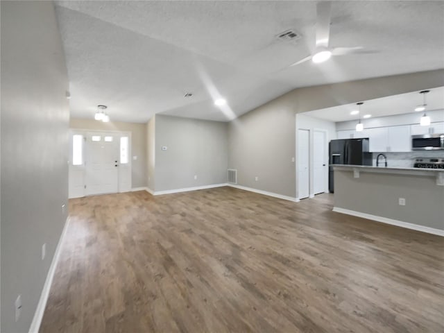 unfurnished living room with baseboards, visible vents, wood finished floors, lofted ceiling, and ceiling fan