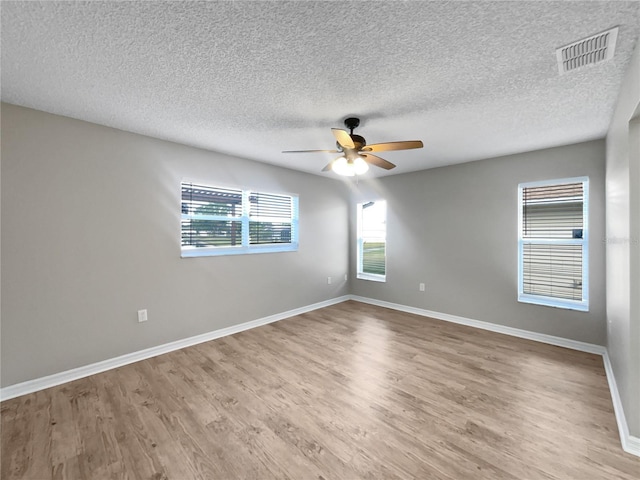 spare room featuring ceiling fan, light wood-type flooring, a textured ceiling, visible vents, and baseboards