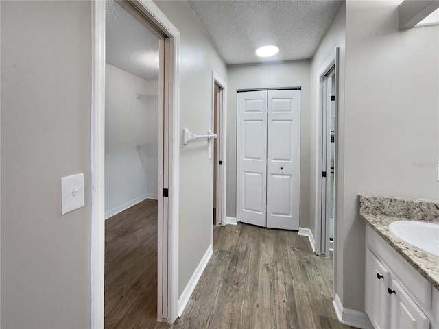 corridor featuring baseboards, a textured ceiling, a sink, and wood finished floors