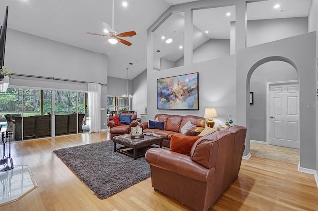 living area featuring high vaulted ceiling, ceiling fan, light wood-style flooring, arched walkways, and baseboards