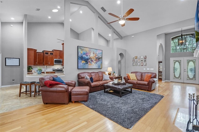 living area with high vaulted ceiling, light wood-style flooring, arched walkways, a ceiling fan, and visible vents