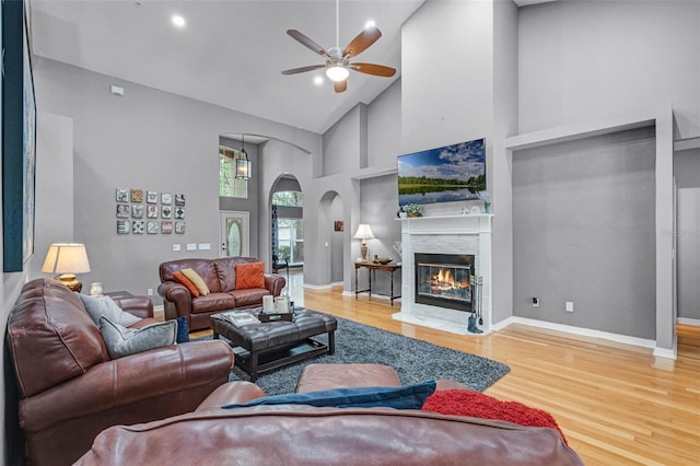 living area with a ceiling fan, wood finished floors, high vaulted ceiling, arched walkways, and a premium fireplace