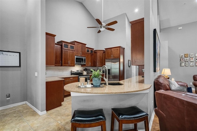 kitchen featuring appliances with stainless steel finishes, a ceiling fan, a kitchen bar, a peninsula, and high vaulted ceiling