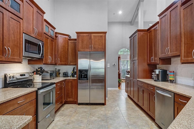 kitchen featuring glass insert cabinets, a high ceiling, appliances with stainless steel finishes, light stone counters, and backsplash