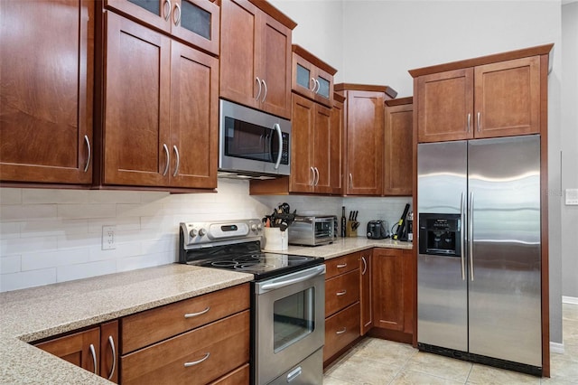 kitchen featuring tasteful backsplash, glass insert cabinets, light stone countertops, a toaster, and stainless steel appliances