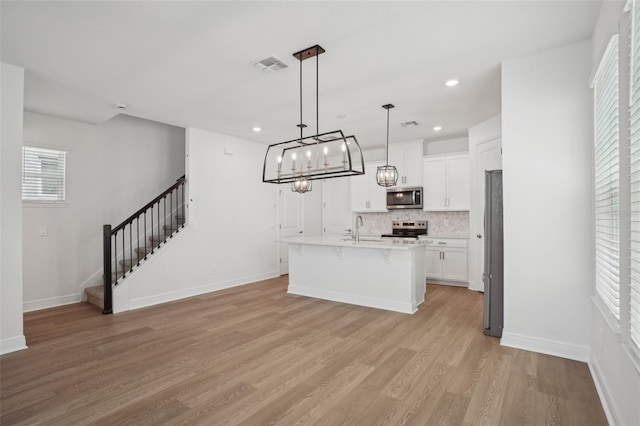 16484 Silver Brook Way, Winter Garden, FL 34787 - kitchen with stainless steel appliances, a sink, light wood-style flooring, a breakfast bar, and white cabinetry