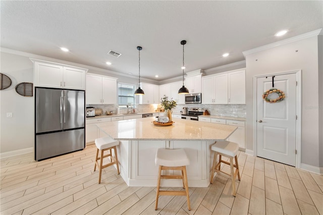 kitchen with visible vents, a center island, a sink, appliances with stainless steel finishes, and white cabinetry