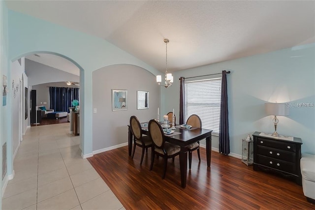 dining room with lofted ceiling, light tile patterned floors, baseboards, arched walkways, and a notable chandelier