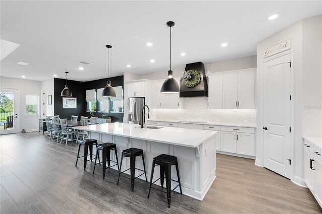 14749 Walcott Ave, Orlando, FL 32827 - kitchen featuring light wood-style flooring, a sink, stainless steel fridge, a center island with sink, and custom range hood