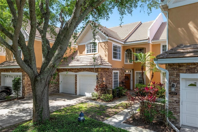 townhome / multi-family property featuring an attached garage, stucco siding, concrete driveway, and stone siding