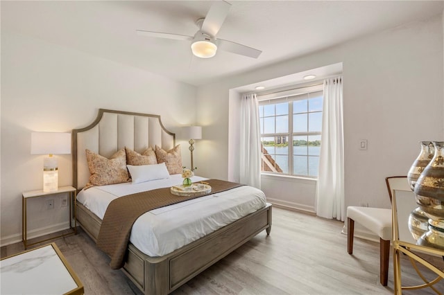 bedroom with light wood-type flooring, a ceiling fan, baseboards, and a water view