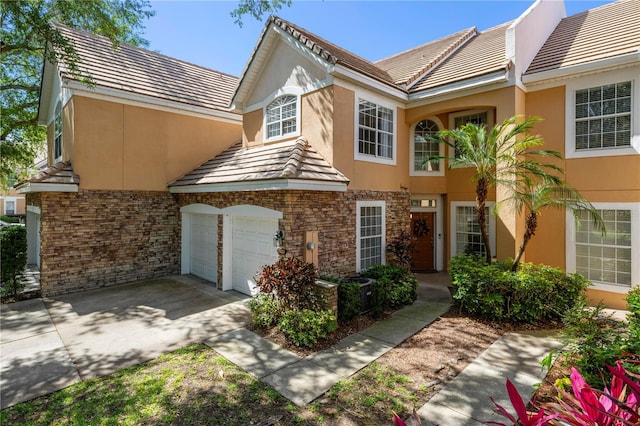 townhome / multi-family property with a garage, stone siding, stucco siding, a tiled roof, and concrete driveway