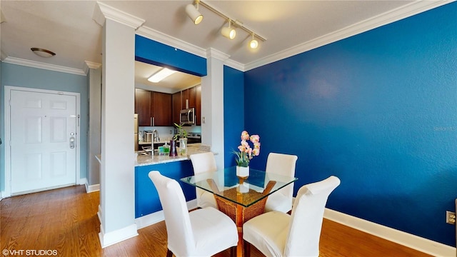 dining space featuring rail lighting, baseboards, ornamental molding, and wood finished floors