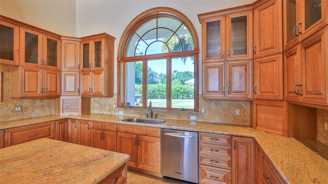 kitchen featuring light stone countertops, brown cabinets, dishwasher, and a sink