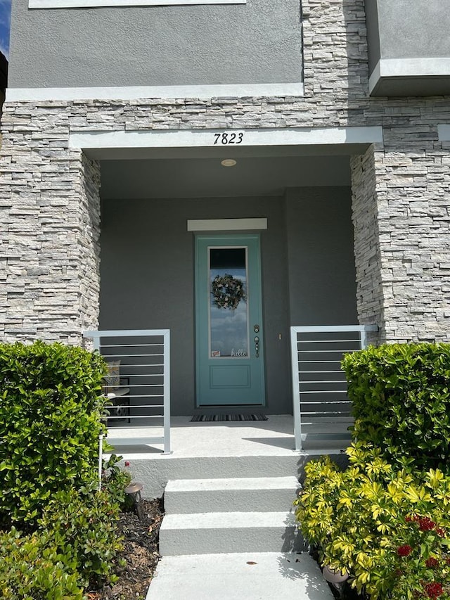 entrance to property featuring a porch, stucco siding, and stone siding