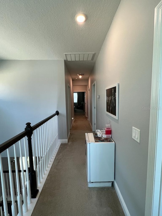hallway featuring a textured ceiling, carpet flooring, baseboards, and visible vents