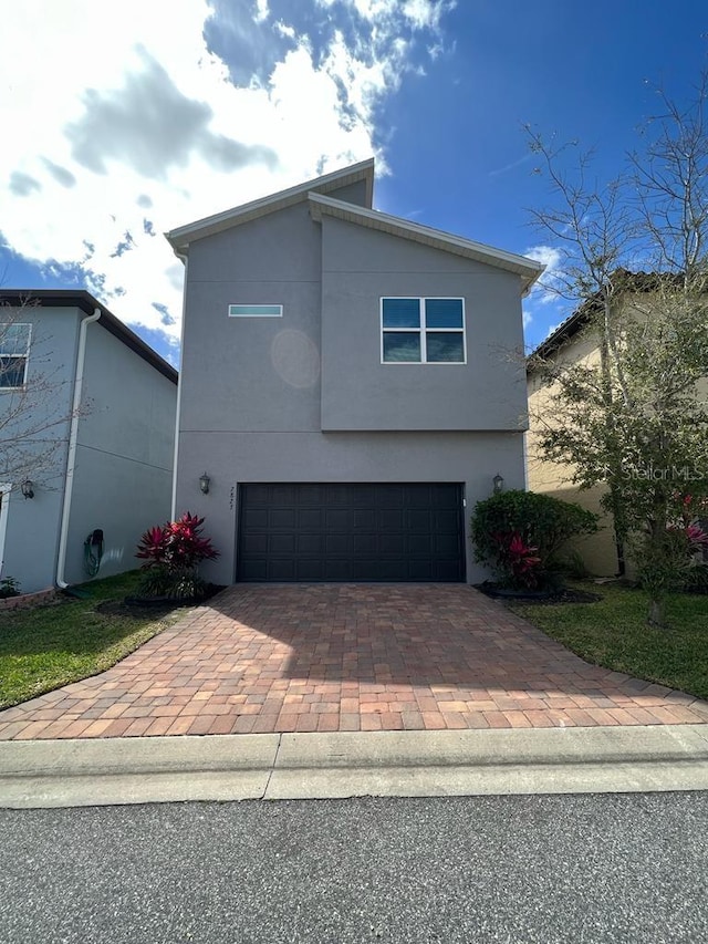 contemporary house with an attached garage, stucco siding, and decorative driveway