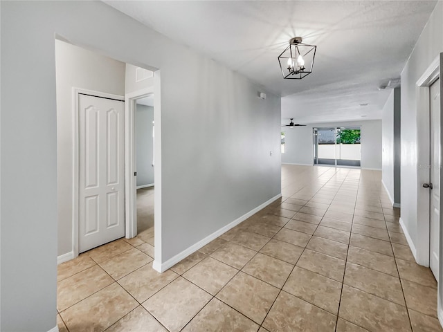 corridor featuring a chandelier, light tile patterned floors, and baseboards