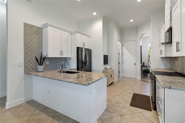 kitchen featuring tasteful backsplash, a sink, arched walkways, stainless steel appliances, and light stone countertops