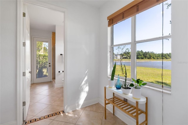 doorway with baseboards, a water view, and light tile patterned flooring