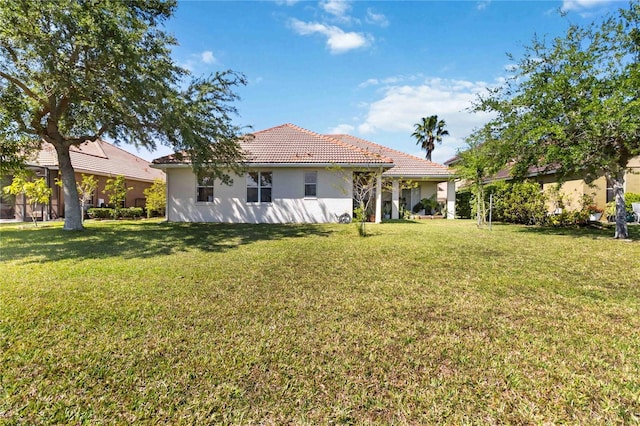 rear view of property featuring a yard, a tile roof, and stucco siding