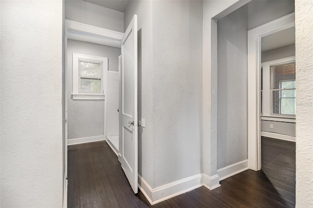 hall featuring baseboards, a textured wall, and dark wood-style flooring