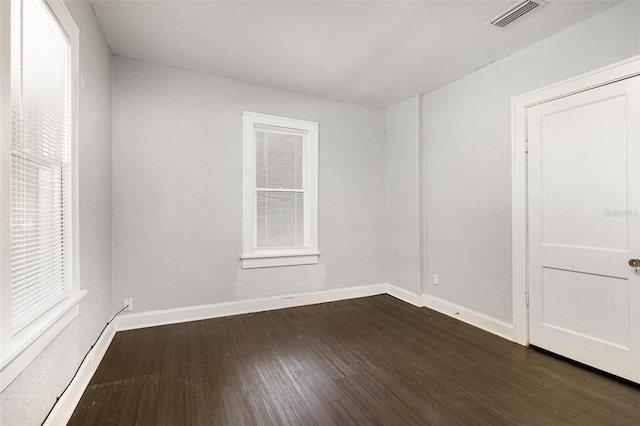 unfurnished room with baseboards, plenty of natural light, dark wood-type flooring, and visible vents
