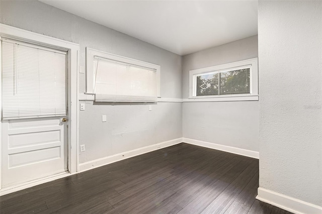 spare room featuring baseboards and dark wood-type flooring