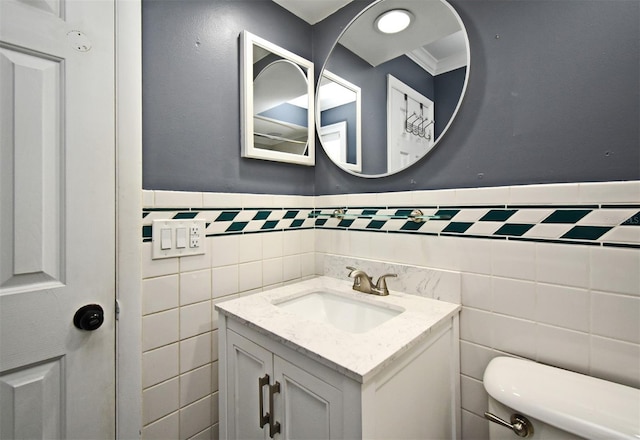 half bath with tile walls, toilet, vanity, and a wainscoted wall