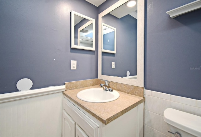 bathroom featuring toilet, vanity, and a wainscoted wall