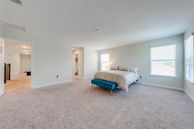 bedroom featuring visible vents, light colored carpet, and a textured ceiling