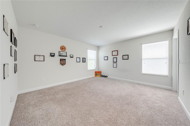 spare room with a textured ceiling, light colored carpet, and baseboards