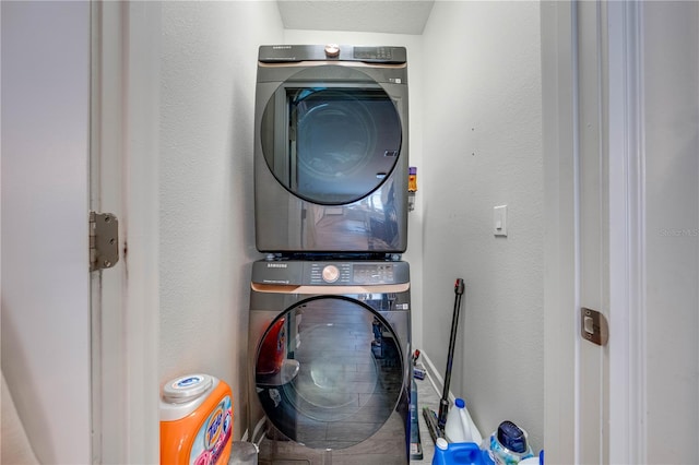 clothes washing area featuring a textured wall, stacked washer and clothes dryer, and laundry area