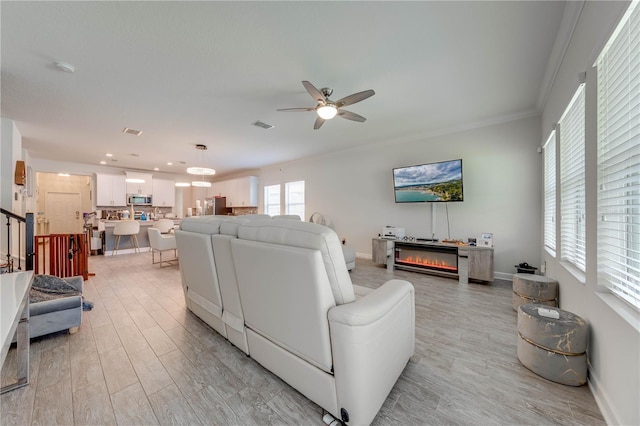 living room with visible vents, baseboards, a ceiling fan, crown molding, and light wood finished floors
