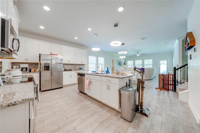 kitchen featuring tasteful backsplash, white cabinets, a center island with sink, stainless steel appliances, and a sink