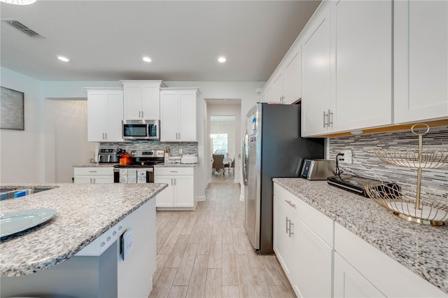 kitchen featuring visible vents, light wood-type flooring, white cabinetry, stainless steel appliances, and backsplash