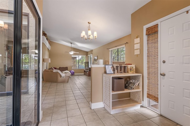 foyer entrance with ceiling fan with notable chandelier, light tile patterned floors, baseboards, and lofted ceiling