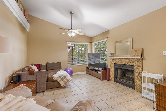 living area featuring ceiling fan, light tile patterned floors, vaulted ceiling, a tiled fireplace, and baseboards