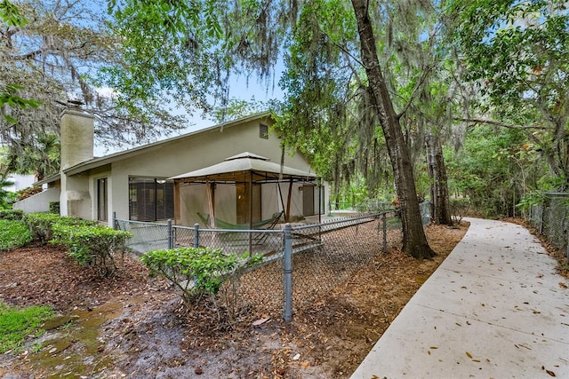 view of home's exterior featuring a gazebo, stucco siding, fence, and a chimney