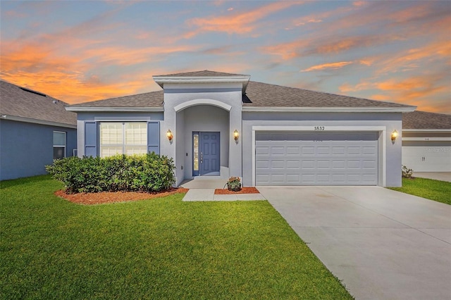 view of front of house featuring a lawn, an attached garage, driveway, and roof with shingles