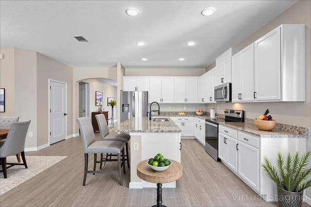 kitchen with appliances with stainless steel finishes, arched walkways, light wood-type flooring, a sink, and white cabinetry