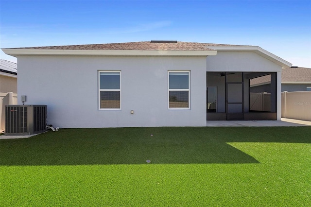 rear view of house with central AC, fence, stucco siding, a sunroom, and a lawn