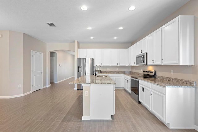 kitchen with a sink, arched walkways, an island with sink, stainless steel appliances, and baseboards