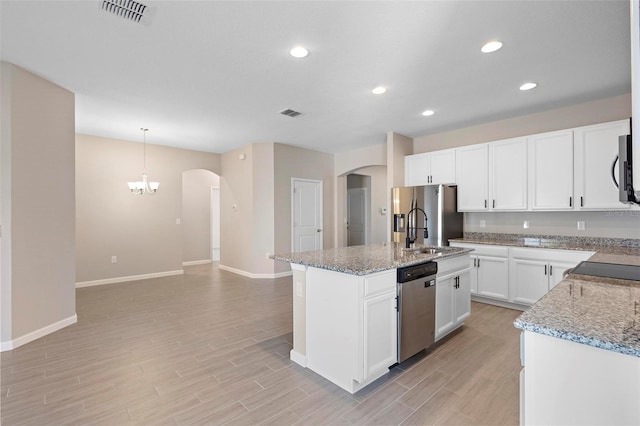 kitchen featuring a kitchen island with sink, visible vents, arched walkways, baseboards, and stainless steel appliances