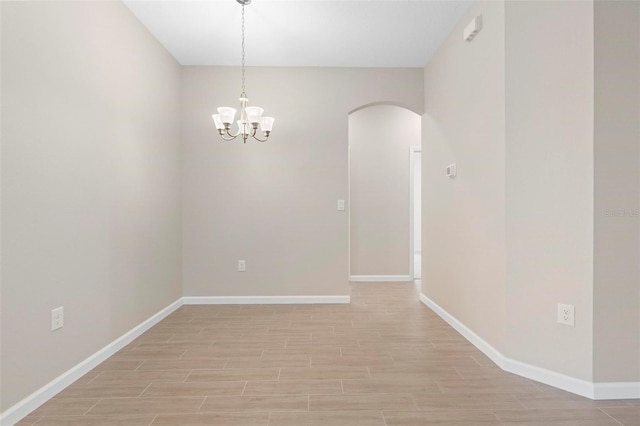 spare room with light wood-style floors, arched walkways, and baseboards