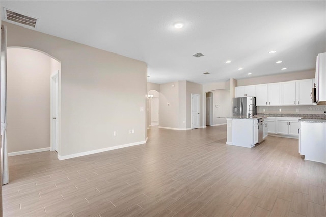 kitchen with visible vents, appliances with stainless steel finishes, arched walkways, a center island with sink, and open floor plan