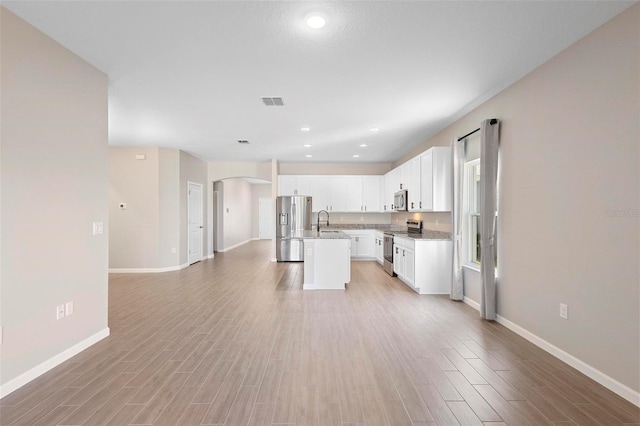 kitchen with baseboards, a center island with sink, arched walkways, a sink, and appliances with stainless steel finishes