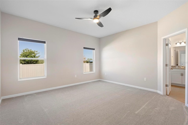 unfurnished bedroom featuring baseboards, ensuite bath, multiple windows, and light carpet