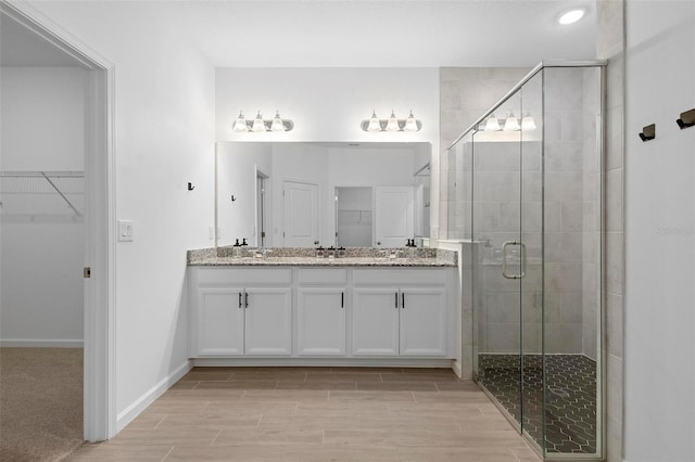 bathroom with double vanity, a walk in closet, and a stall shower