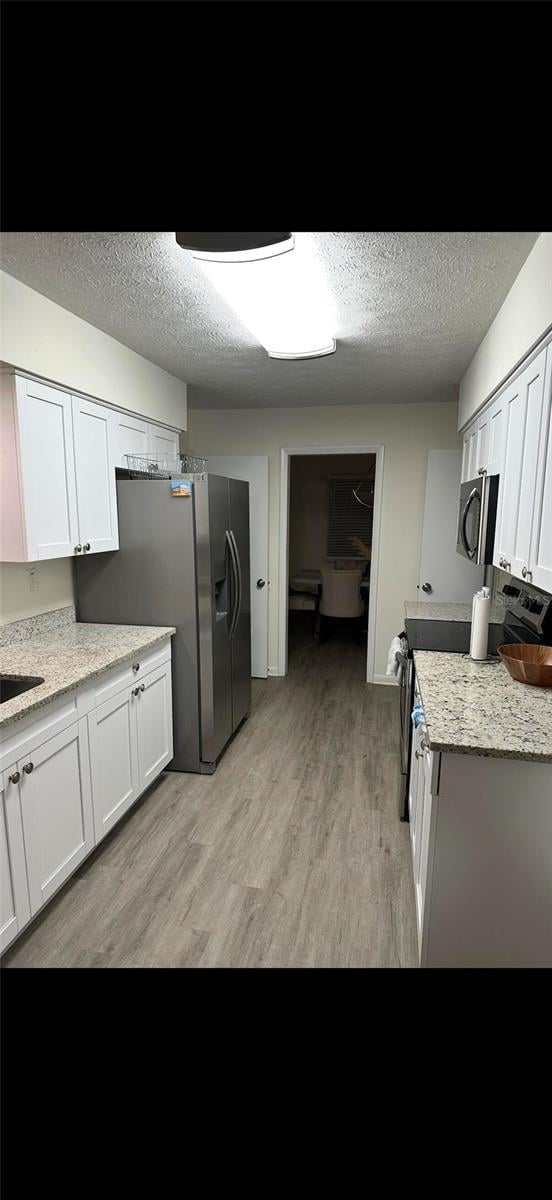 2902 Little Rd, Valrico, FL 33596 - kitchen featuring white cabinets, appliances with stainless steel finishes, light wood-style floors, a textured ceiling, and light stone counters
